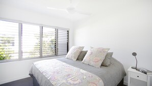 A bedroom with a bed, a nightstand, a ceiling fan, and a window with blinds. - Ocean Views at Sandrift on Nobby Beach (Gold Coast)