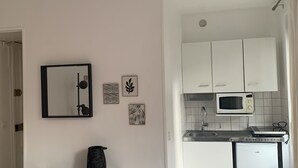 Cocina moderna con armarios blancos, un microondas y un lavamanos. Hay un mueble negro con un jarrón texturizado encima.