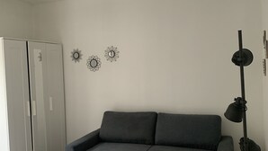Una habitación con un sofá gris, una lámpara de pie alta y un armario.