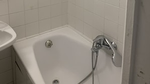 Un baño pequeño con azulejos blancos, una bañera, un perchero rojo y un lavamanos blanco.