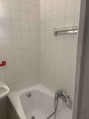 Um banheiro pequeno com azulejos brancos, uma banheira, um porta-toalhas vermelho e uma pia branca.