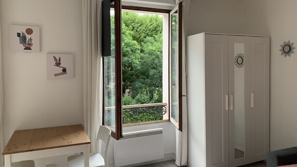 Un dormitorio con un escritorio de madera, una silla blanca, un armario y una ventana con cortinas.