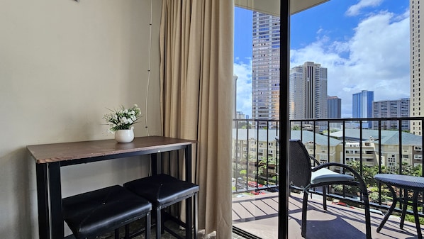 A balcony with a view of tall buildings, a table with two chairs, and a potted plant.