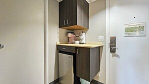 Una kitchenette compacta con refrigerador, cafetera y una pequeña encimera.