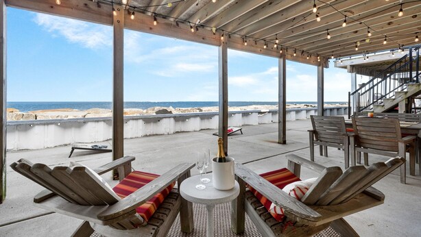 Un espacio de estar al aire libre cubierto con sillas y mesas de madera, con vista a la playa.