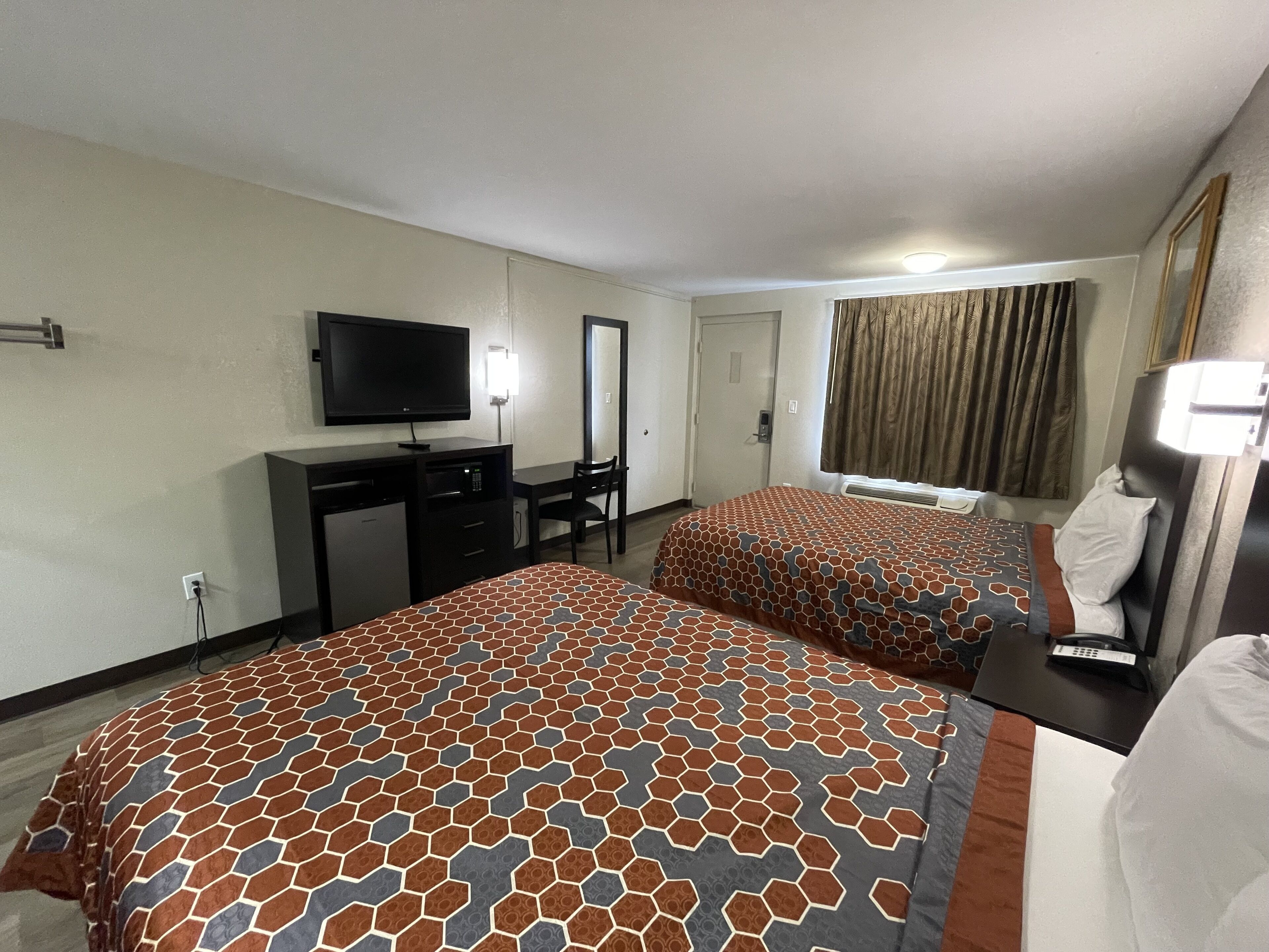A hotel room with two beds, a desk, a television, and a mirror.