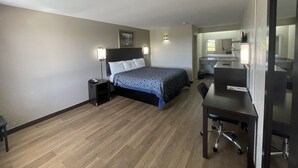 A hotel room with a bed, bedside lamps, a desk with a chair, and a bathroom visible through an open door. - Royal Inn Motel (Fredericksburg)