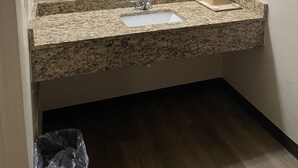 A bathroom with a granite countertop, a sink, a mirror, a towel rack, and a trash bin. - Royal Inn Motel (Fredericksburg)