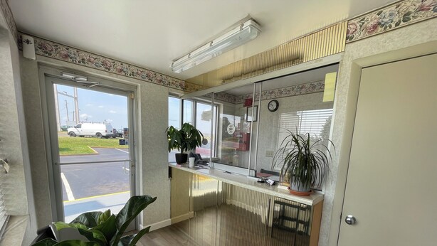 A reception area with a counter, potted plants, a clock, and a view of the parking lot. - Royal Inn Motel (Fredericksburg)