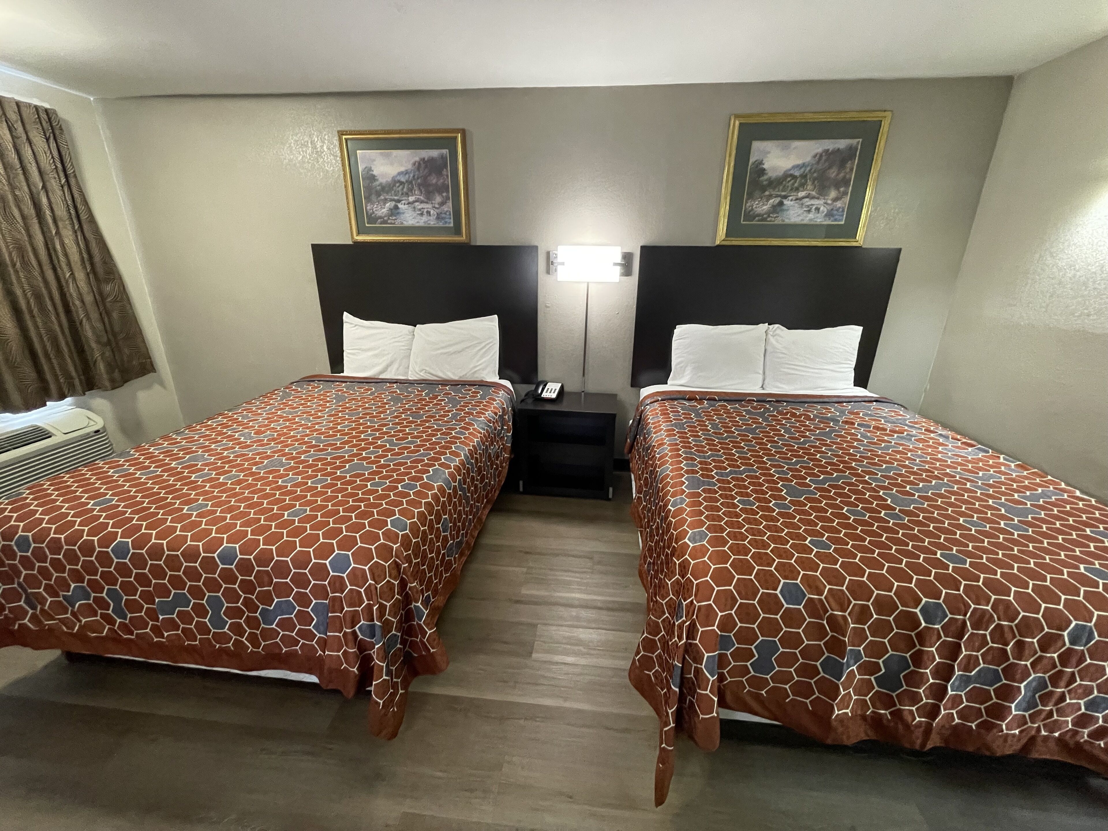 A hotel room with two beds, each with a patterned bedspread, a nightstand, a lamp, and two framed pictures on the wall.