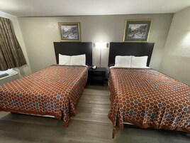 A hotel room with two beds, each with a patterned bedspread, a nightstand, a lamp, and two framed pictures on the wall.