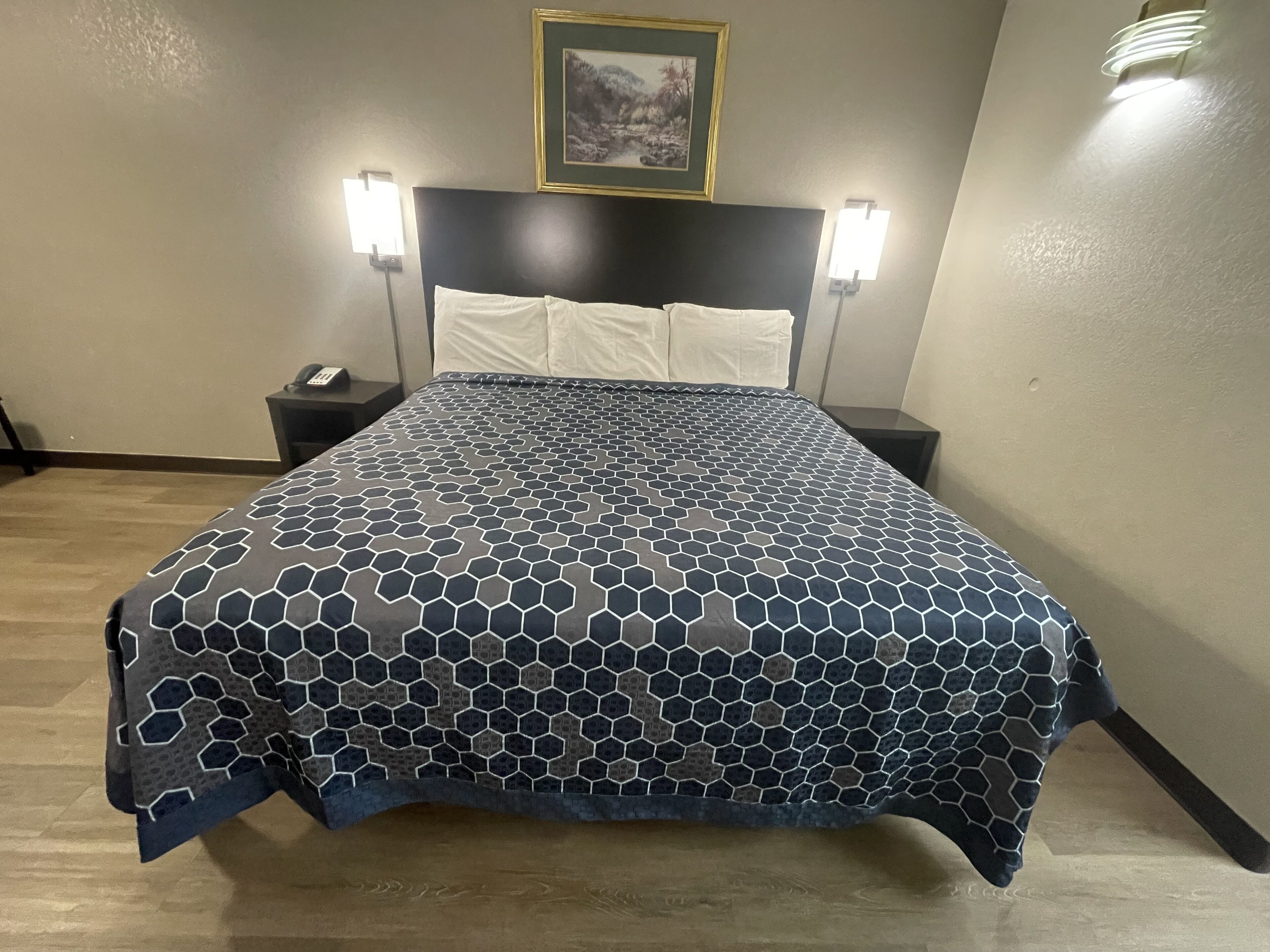 A hotel room with a large bed, two bedside tables, a nightstand, a framed picture on the wall, and two wall-mounted lamps.