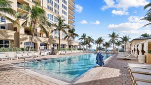 A pool area with lounge chairs, palm trees, and a building with balconies. - Ocean View 1 Bedroom Condo (Singer Island)