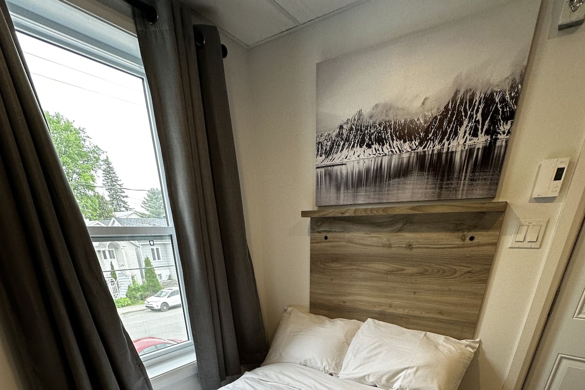 A bedroom with a bed, a window with curtains, a wall-mounted artwork, and a door.