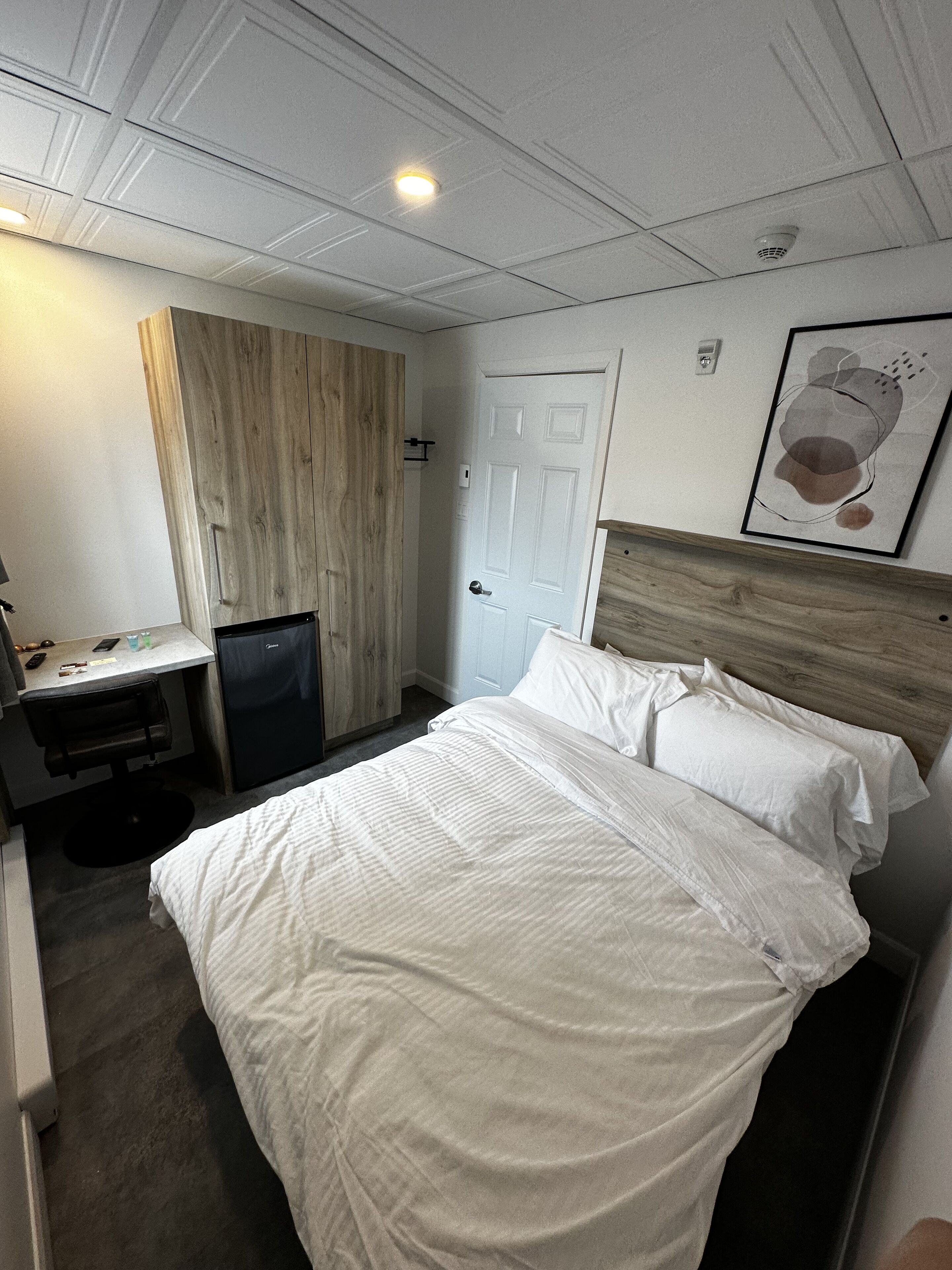 Una habitación de hotel con cama, escritorio, silla, refrigerador y puerta.
