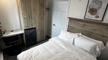 Una habitación de hotel con cama, escritorio, silla, refrigerador y puerta.