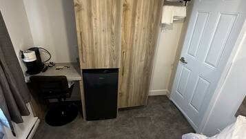 A hotel room with a bed, a desk with a computer, a small refrigerator, a wardrobe, and a door.