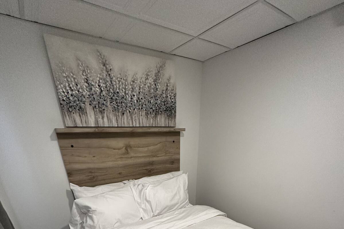 A neatly made bed with white bedding in a room with a wooden headboard and a wall-mounted painting of flowers.
