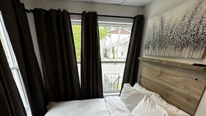 Ein Bett mit weißer Bettwäsche, einem Holzkopfende und dunklen Vorhängen.