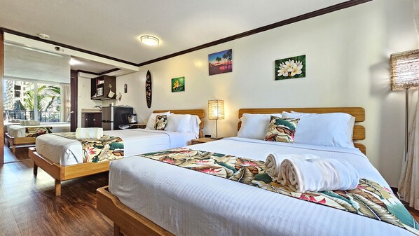 Une chambre d’hôtel avec deux lits, une grande fenêtre, une kitchenette et des œuvres d’art accrochées aux murs.
