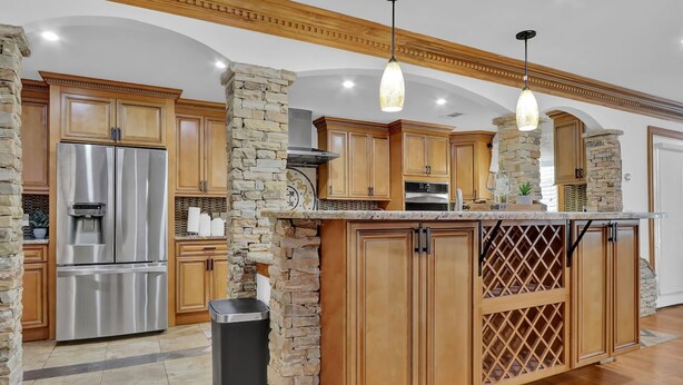 Una cucina con mobili in legno, un frigorifero in acciaio inossidabile e una parete decorativa in pietra.