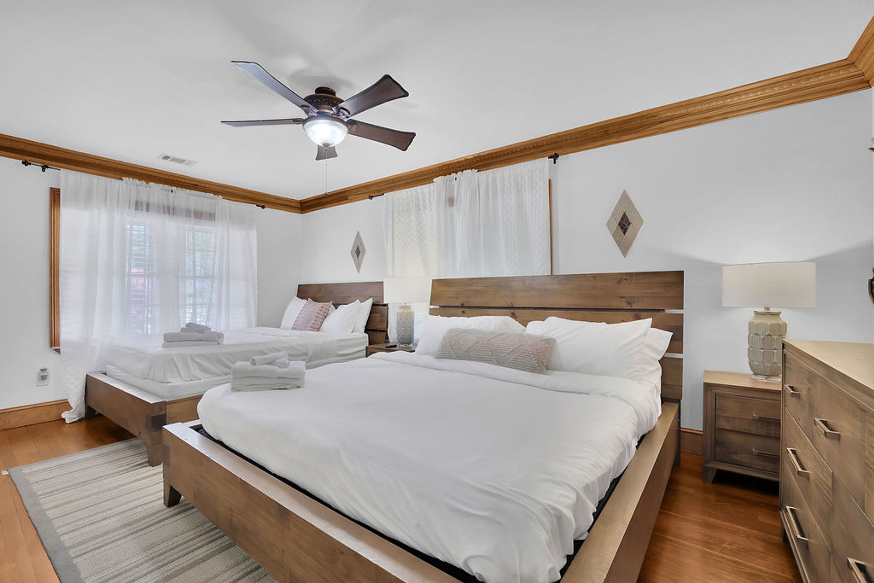 A bedroom with two beds, wooden headboards, a ceiling fan, and a nightstand with a lamp.