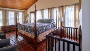 A spacious bedroom with a four-poster bed, wooden ceiling, and large windows with curtains.