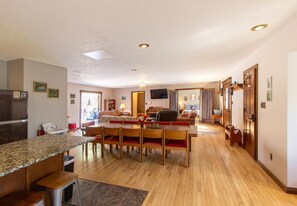 A spacious living area with a wooden dining table, chairs, a kitchen area with a refrigerator, and a television mounted on the wall. - Private Retreat w Pool Hot Tub and Dining Hall (Bloomington)