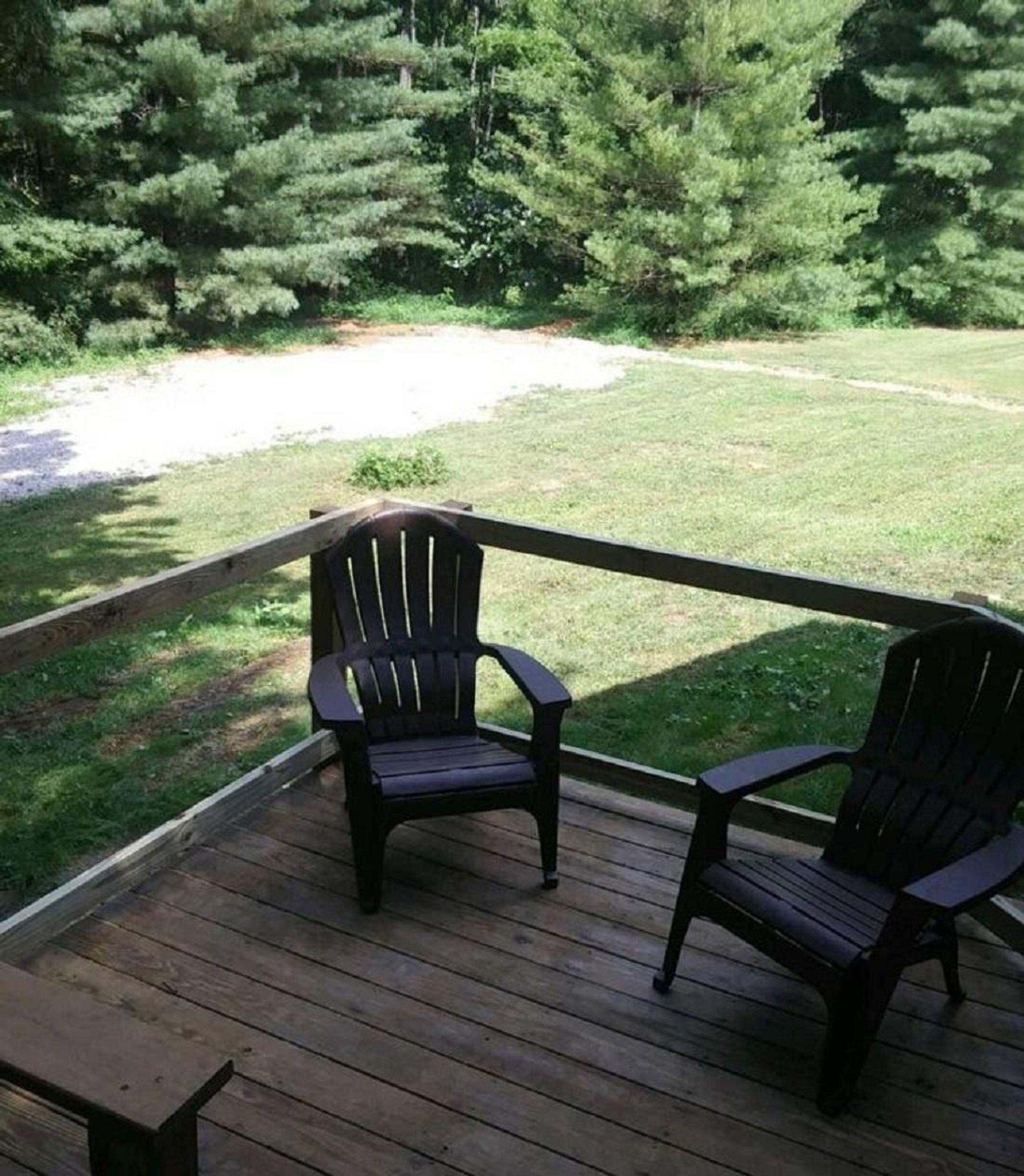 Una terraza de madera con dos sillas Adirondack mirando hacia un espacio cubierto de césped y un fondo boscoso.