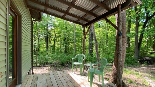 A wooden deck with two green chairs and a table, surrounded by a forest.