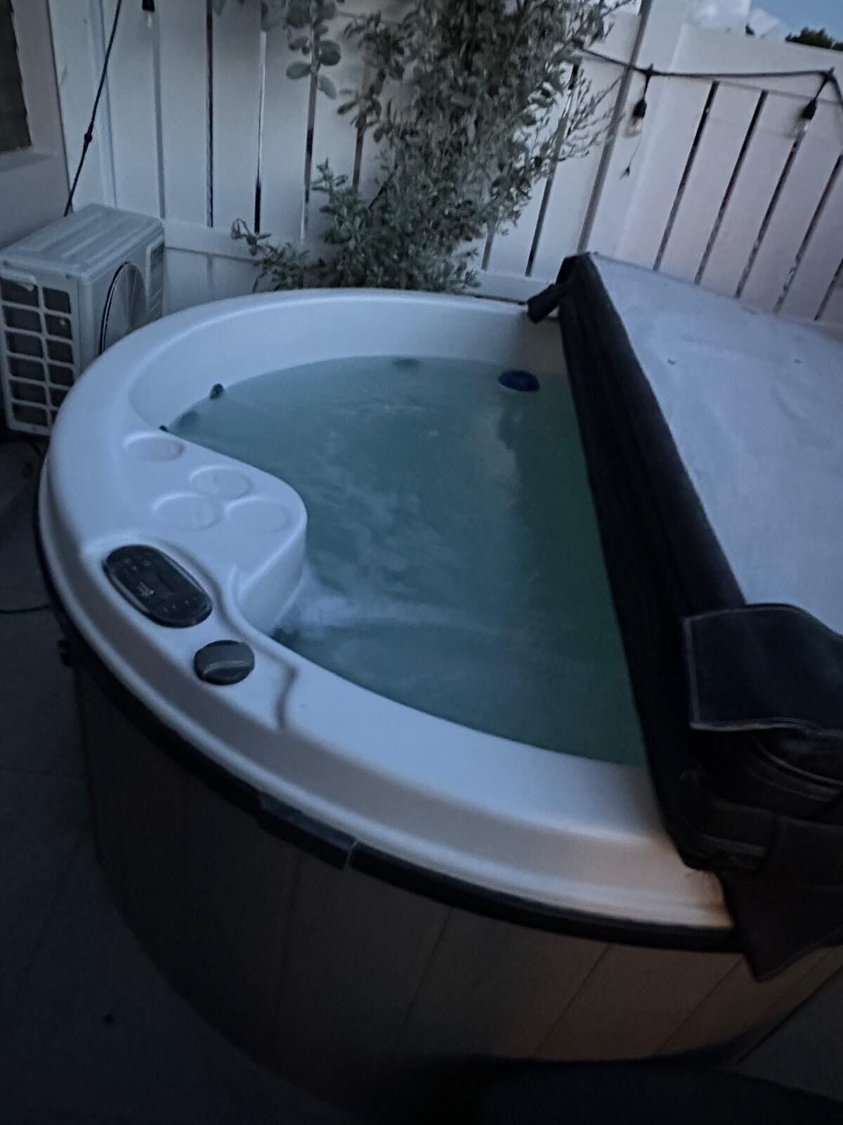Un jacuzzi con panel de control, una cubierta y una planta cerca.