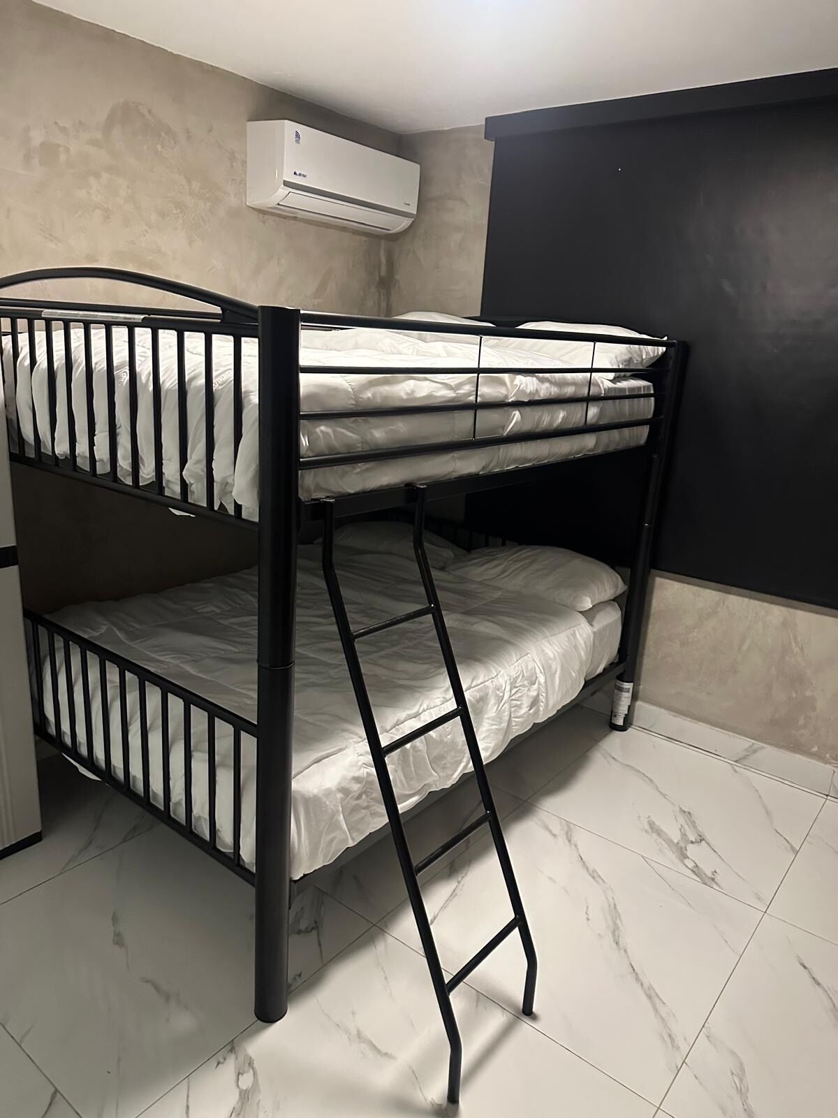 A bunk bed with a ladder, white bedding, and an air conditioner mounted on the wall.