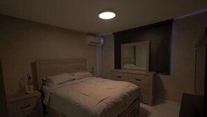 Een slaapkamer met een bed, nachtkastje, kaptafel en een spiegel aan de muur.
