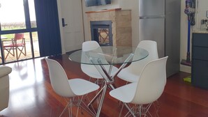 Une cuisine moderne avec une table à manger au plateau en verre, des chaises blanches, un four encastré et un téléviseur à écran plat placé au-dessus du plan de travail.