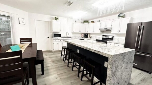 A modern kitchen with white cabinets, a granite island, and stainless steel appliances. - D'Oasis "Pool Paradise" Hot tub, Sleeps15 Pet friendly, Come Celebrate BOOK IT!  (San Antonio)
