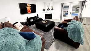 A modern living room with a flat-screen TV, a fireplace, leather sofas, and a view of the outdoors. - D'Oasis "Pool Paradise" Hot tub, Sleeps15 Pet friendly, Come Celebrate BOOK IT!  (San Antonio)