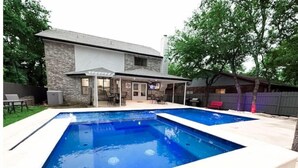 A residential backyard with a rectangular swimming pool and a covered patio area. - D'Oasis "Pool Paradise" Hot tub, Sleeps15 Pet friendly, Come Celebrate BOOK IT!  (San Antonio)