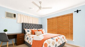 A bedroom with a bed, a desk, a chair, a ceiling fan, and a window with blinds.