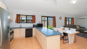 A modern kitchen with a central island, a dining area with a table and chairs, a sofa, and a ceiling fan.