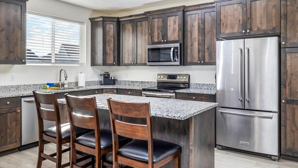 A kitchen with dark wooden cabinets, stainless steel appliances, granite countertops, and a central island with bar stools. - Beautiful home at Bear Lake sleeps 20+ with access to Ideal Beach included (Garden City)