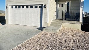 A two-story house with a garage, a front porch with steps, and a small outdoor seating area. - Beautiful home at Bear Lake sleeps 20+ with access to Ideal Beach included (Garden City)