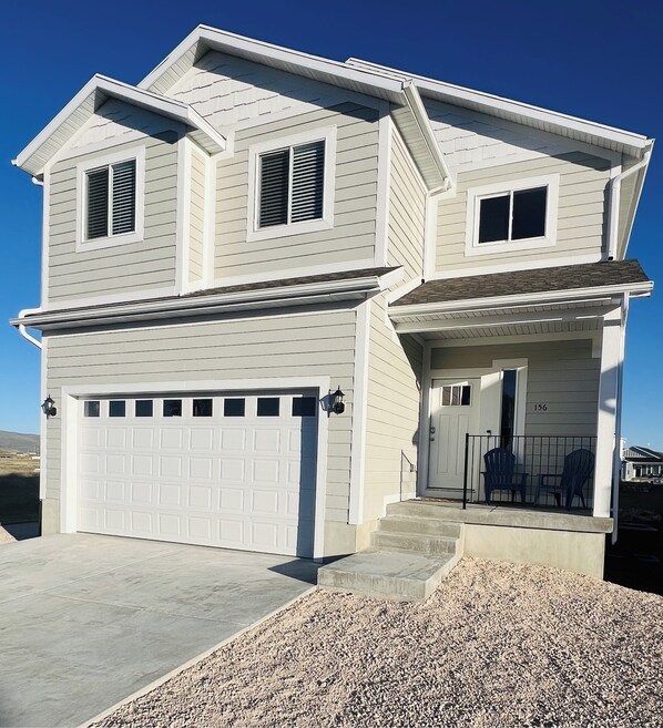 A two-story house with a garage, a front porch with steps, and a small outdoor seating area. - Beautiful home at Bear Lake sleeps 20+ with access to Ideal Beach included (Garden City)