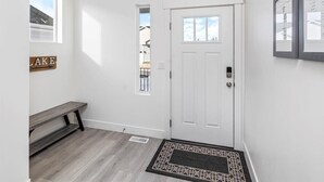 A clean, white-walled hallway with a wooden bench, a white door with a small window, and a framed picture on the wall. - Beautiful home at Bear Lake sleeps 20+ with access to Ideal Beach included (Garden City)