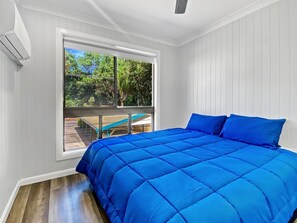 A bedroom with a large bed, a window with a view of greenery, and a balcony with outdoor furniture. - Magnetic Reef Unit 2 (Arcadia)