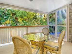 A glass-top table with wicker chairs on a balcony with a view of lush greenery. - Magnetic Reef Unit 2 (Arcadia)