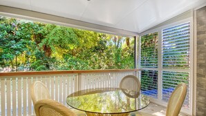 Een glazen tafel met rieten stoelen op een balkon, met uitzicht op weelderige begroeiing.