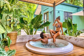 A hot tub with a wooden deck and tropical plants.