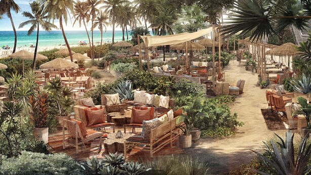 Zona salotto all'aperto con tavoli e sedie, circondata da piante tropicali e palme, che conduce a una spiaggia.