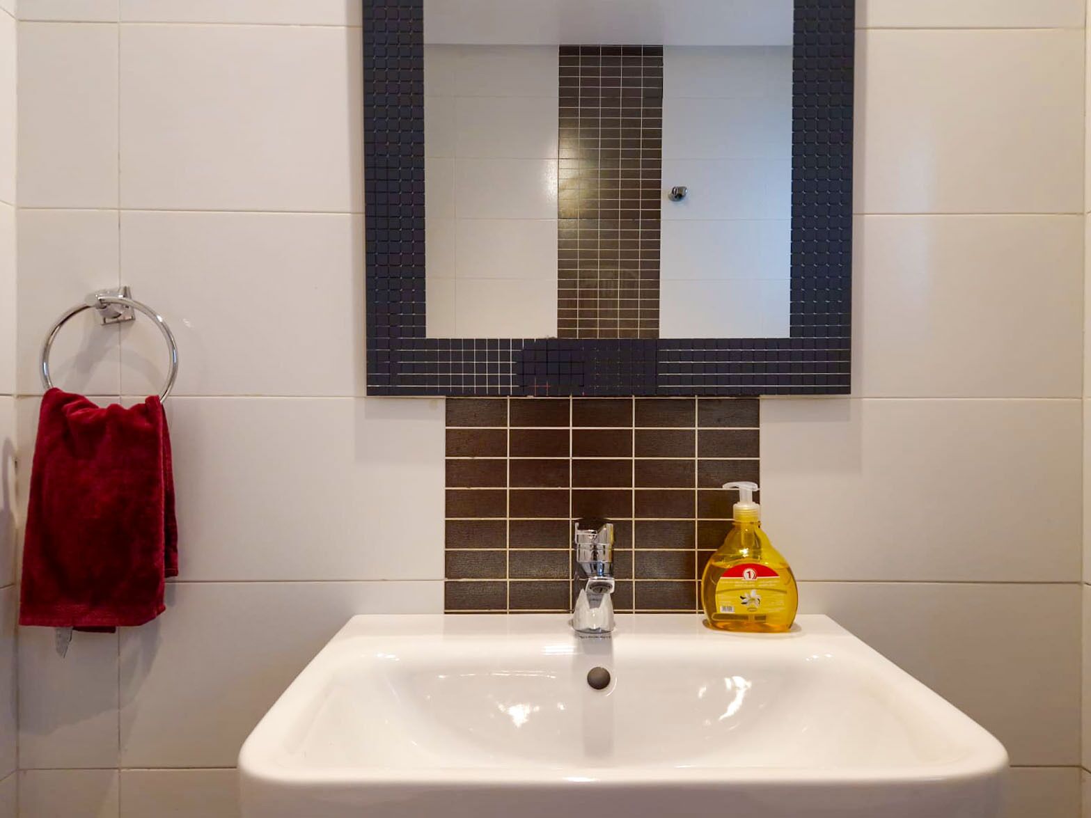 Un baño con un lavabo blanco, un espejo con marco oscuro y una toalla roja colgada en un aro metálico.
