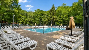 Una piscina con sillas de descanso blancas y sombrillas, rodeada de árboles.